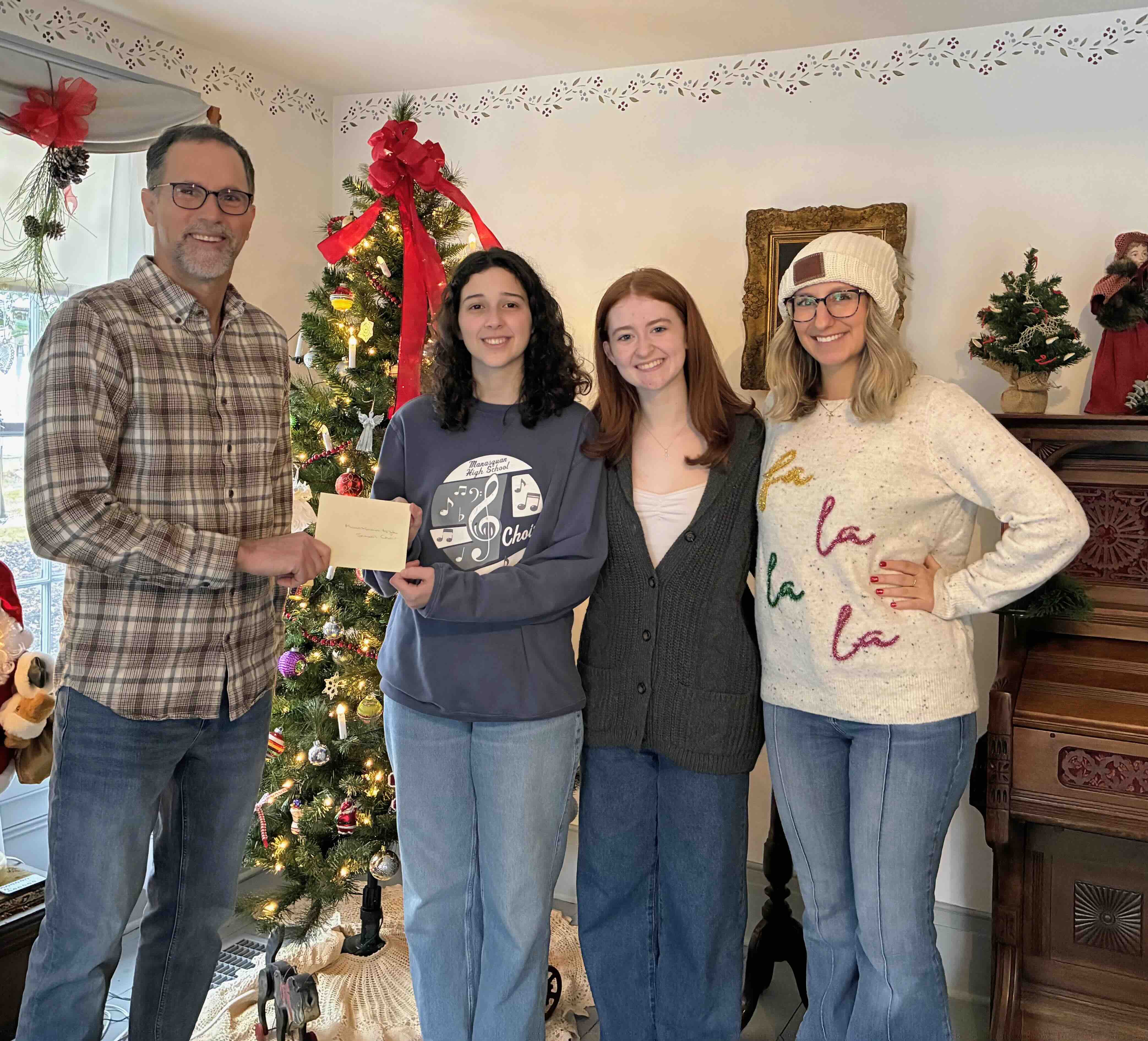 Four people standing in front of a decorated Christmas tree during a check presentation.