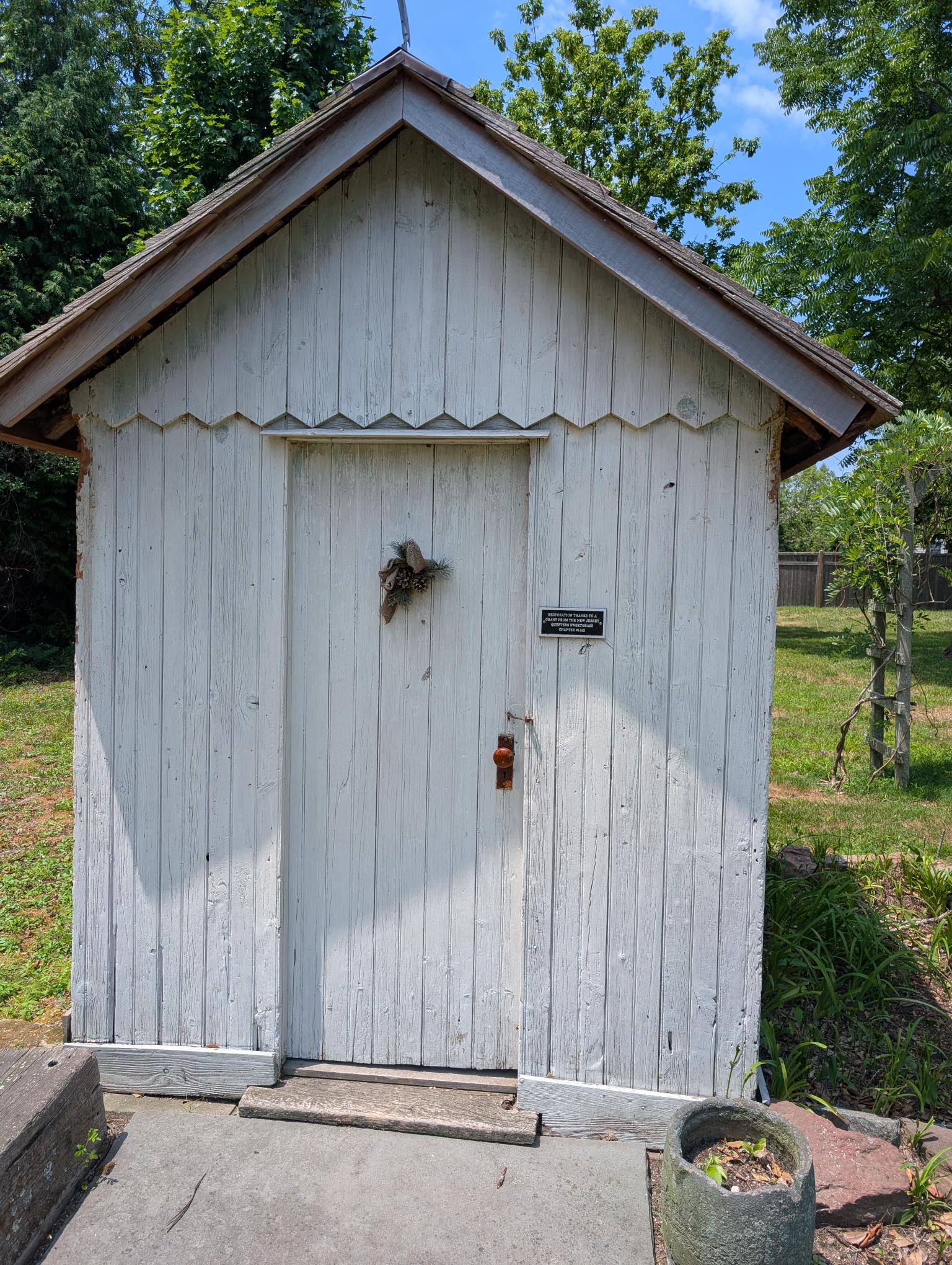 Exterior image of a wooden white outhouse with a peaked roof. 
